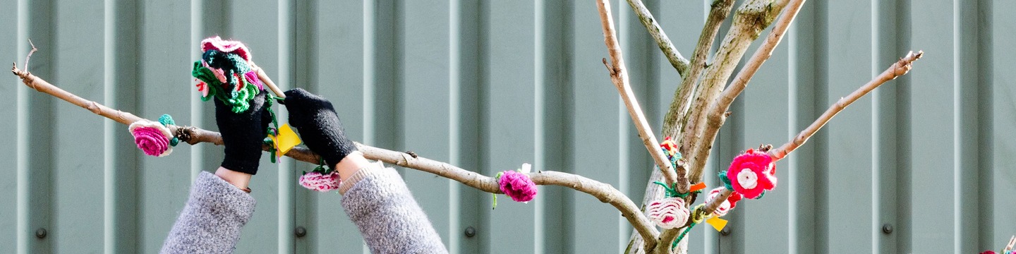 Iemand hand gehaakte bloemen aan een kale boom